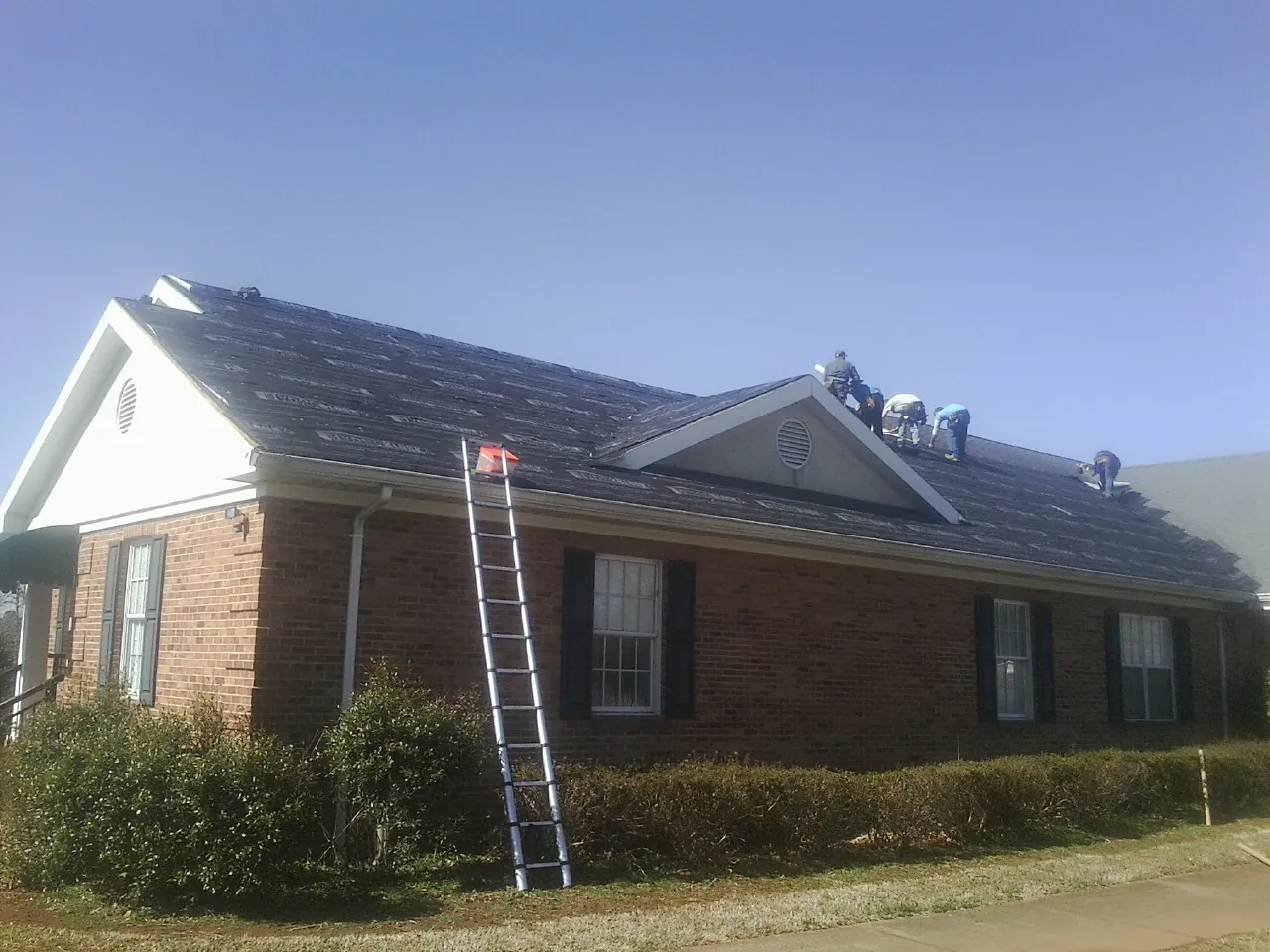 Crew tearing shingles off a brick ranch roof with a ladder set — Emergency Roof Repair work by our crew in Orcas