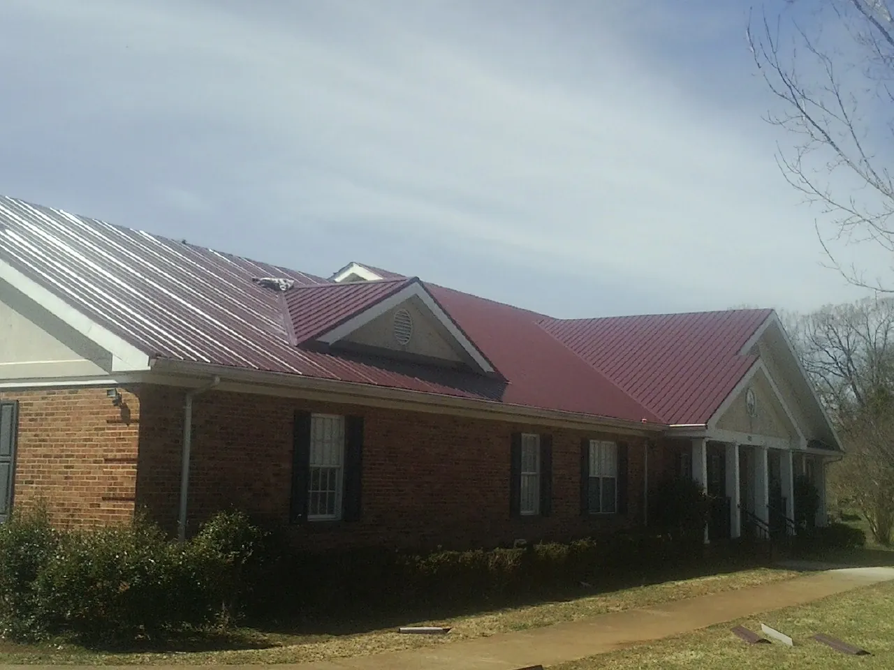 Red metal roof with gabled entries on a long brick building, from a Hail Damage Roof Repair job in Orcas