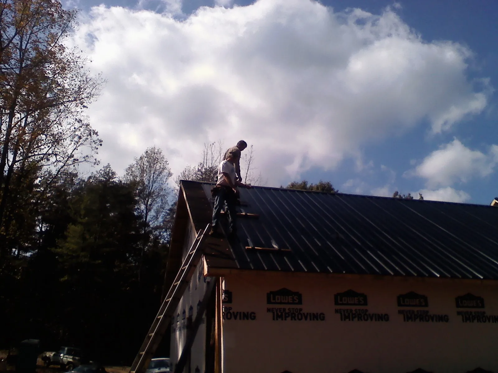 Roofer fastening dark metal panels high against a cloudy sky, from a Roof Inspection job in Orcas